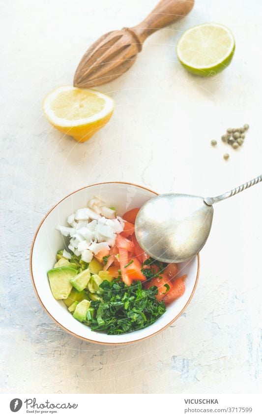 Schüssel mit Löffel und frischen Zutaten: Avocado, Koriander, Tomate, Zwiebel. Gesundes Essen Konzept.  Weißer Hintergrund. Ansicht von oben Schalen & Schüsseln