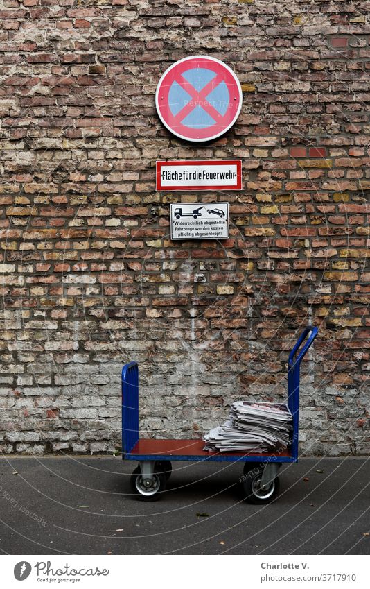 Hochkant im Halteverbot | Handwagen mit Zeitungen vor Ziegelwand mit Haltverbotsschild transportwagen zeitungen Zeitungsstapel Halteverbotsschild