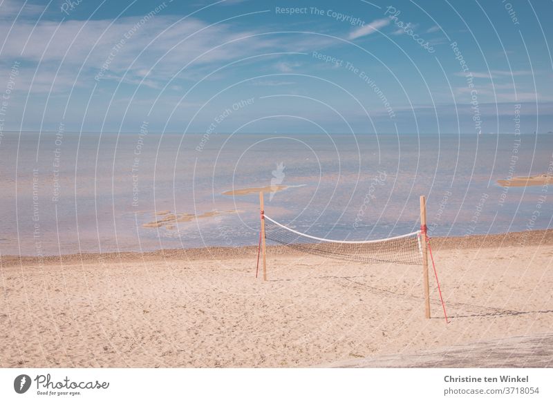 Leerer Nordseestrand mit Volleyball / Beachball Netz  direkt am Wasser. Sonnenschein, blauer Himmel, einige Wolken und Horizont. Strand Beachballnetz