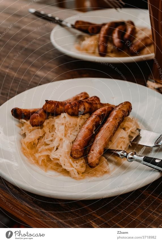 Schweinswürste mit Kraut kraut sauerkraut ernährung tradition bayern wurstwaren metzger Metzgerei besteck teller sommer sonne holztisch biergarten restaurant