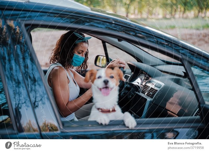 junge frau mit schutzmaske in einem auto. daneben süßer jack russell hund. Reisen und neues normales Konzept Frau Hund PKW Schutzmaske Corona-Virus neue Normale