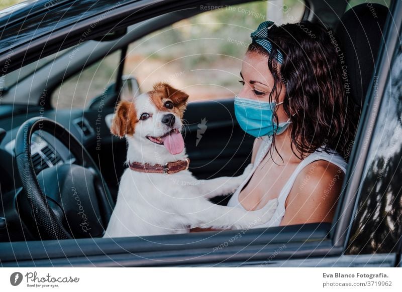 junge frau mit schutzmaske in einem auto. daneben süßer jack russell hund. Reisen und neues normales Konzept Frau Hund PKW Schutzmaske Corona-Virus neue Normale