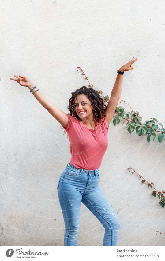 Junge Frauen mit erhobenen Händen bleiben in der Nähe einer Wand jung Mädchen anhaben nach oben Attrappe T-Shirt Jeanshose Aufenthalt Lächeln Rundhals