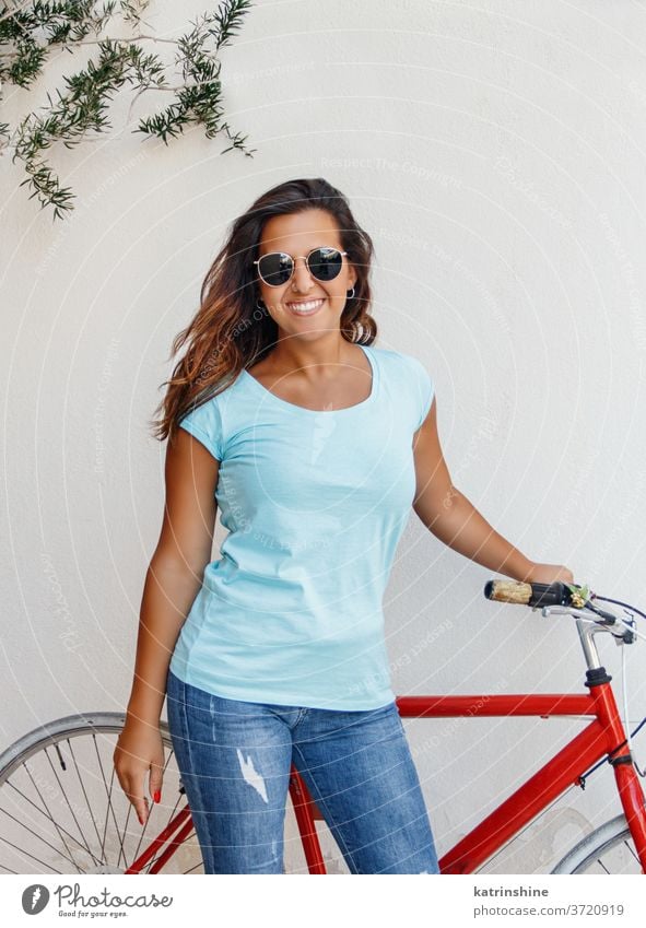 Junge Frauen mit Fahrrad halten sich in der Nähe einer Mauer auf jung Mädchen anhaben Attrappe T-Shirt Jeanshose Aufenthalt Wand Lächeln Rundhals