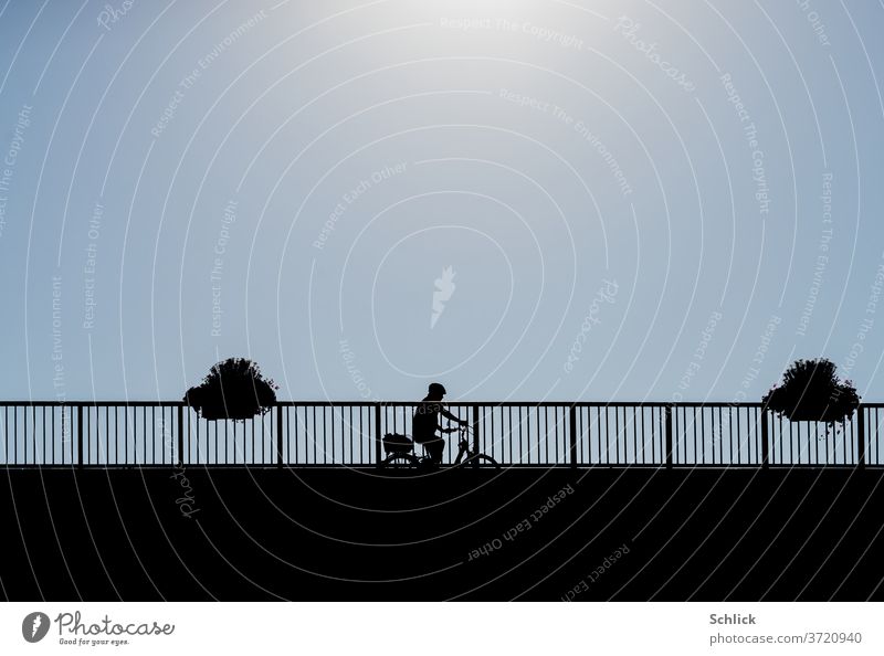 Radfahrer fährt unter Sommerhitze über Brücke Himmel blau Silhouette Hitze Blumenkästen Froschperspektive Fahrradhelm Sonne Geländer schwarz Mensch ein