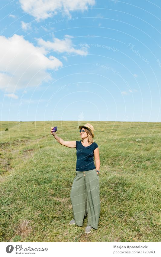 Junge Frau, die im Sommer auf einer Wiese am Hang ein Selfie macht Erwachsener Abenteuer schön Blog Blogger bloggend Fotokamera Kaukasier heiter Land niedlich