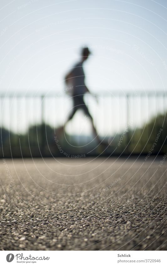 Mann geht vor Geländer über Asphalt starke Unschärfe Mensch gehen unscharf Gegenlicht Himmel blau Profil Seitenansicht schreiten Bewegung out of focus