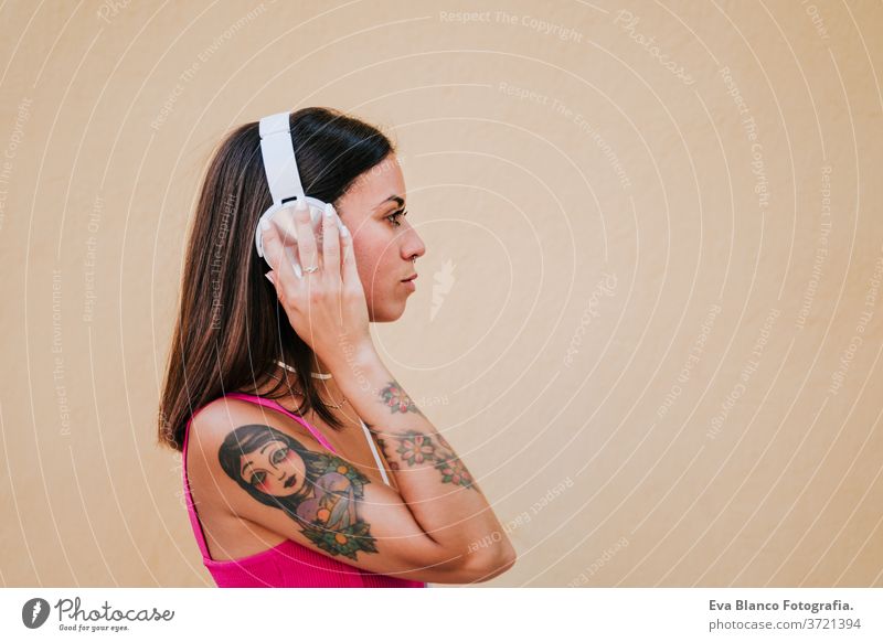 Fröhliche junge Frau im Freien, die mit Handy und Headset Musik hört. Technologie und Lebensstil Musik hören Glück Tattoo Technik & Technologie Großstadt urban