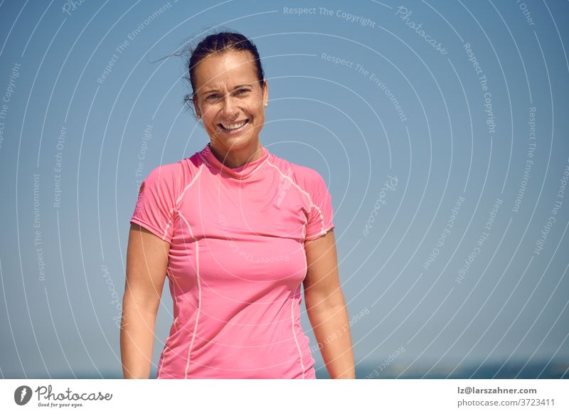 Glücklich lächelnde, attraktive, athletische, schlanke Frau mittleren Alters, die mit einem warmen, freundlichen Lächeln in die Kamera auf einen sonnigen, blauen Sommerhimmel mit Kopierraum blickt