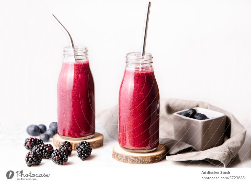 Beeren-Smoothie in Glasflaschen mit wiederverwendbaren Metallstrohhalmen. Frontalaufnahme mit weißem Hintergrund. Flasche Farbe trinken Essen und Trinken