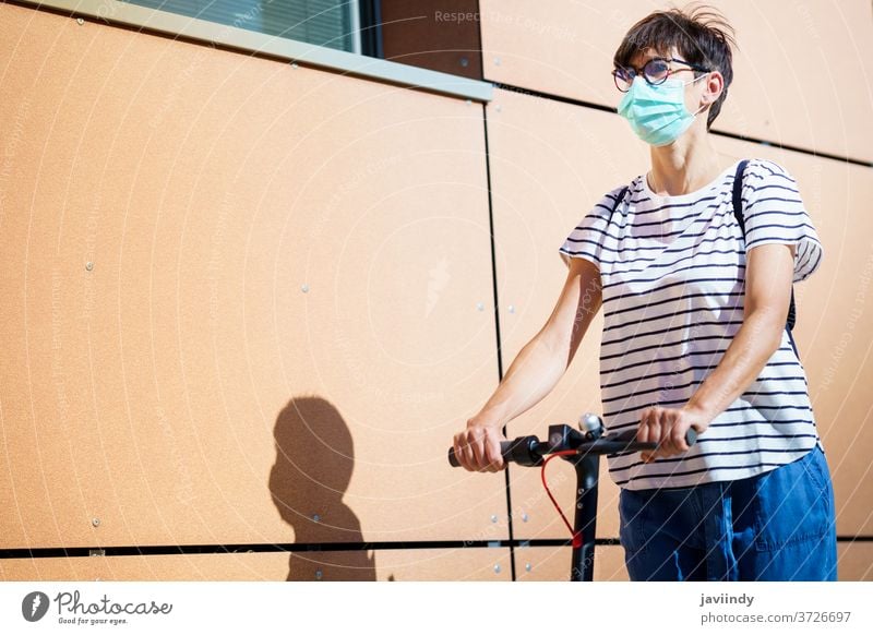 Frau fährt auf einem Elektroroller durch die Stadt Tretroller elektrisch Mädchen Mundschutz Öko Transport urban Lifestyle modern Freizeit Großstadt