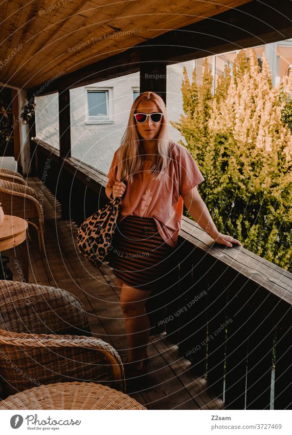 Junge Frau auf dem Balkon einer Ferienwohnung ferien urlaub wohnen balkon sonnebrille Mädchen blond hübsch tasche sommer wärme garten zuhause grün büsche rock