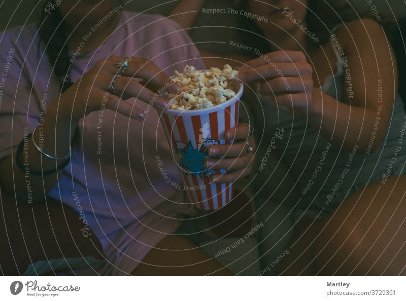 Junge Frauen bekommen Popcorn und sehen sich am Wochenende online einen Film an, während sie zusammen auf dem Sofa in einem gemütlichen Wohnzimmer sitzen.