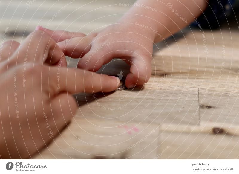 Eine Hand gibt, die andere nimmt. Mutter schiebt ihrem Kind eine Geldmünze über den Holztisch zu. geldmünze kind schieben geben nehmen kosten teuer kindergeld