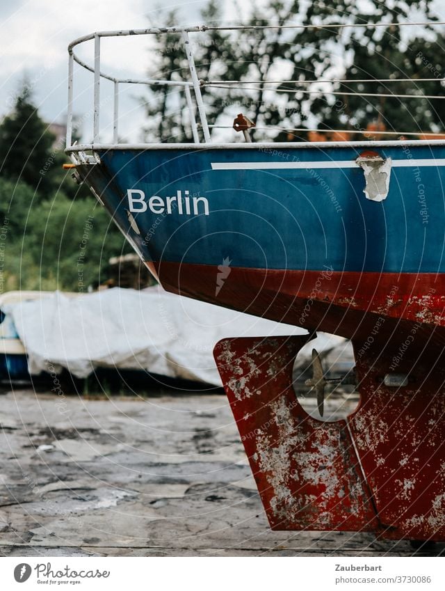 Heck mit Ruder eines alten Motorboots in rot und blau an Land aus Berlin Boot Rost verrostet Lager Bootslager Bock aufgebockt Schiff Schiffsfriedhof ausgedient