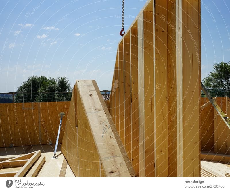 Baustelle Holzbau, eine Hauswand hängt am Kran Holzhaus Zimmerei Farbfoto Außenaufnahme Handwerk Textfreiraum oben Hausbau Fassade Gebäude Handwerker bauen