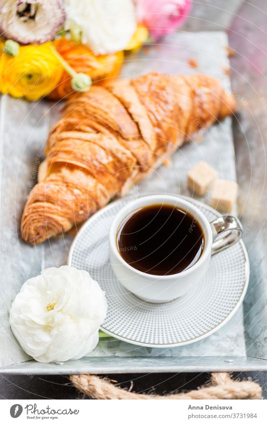 Frisches Croissant, Tasse Kaffee und Hahnenfußblüten. Frühstück Morgen Gebäck weiß Tisch Ranunculus Blumen trinken Tablett Espresso süß schwarz Cappuccino