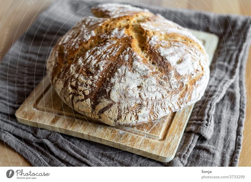 Frisch gebackener Brotlaib mit Kruste auf einem Holz Schneidebrett frisch knusprig geschirrtuch Lebensmittel rustikal Bäckerei Frühstück Gesunde Ernährung