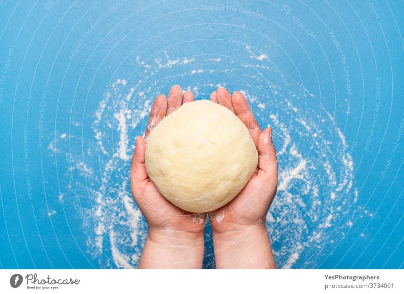 Brotteig in der Hand über einen blauen Tisch halten. Ungekochter Teig. Backen zu Hause Hintergrund backen Bäckerei Brötchen Konzept Essen zubereiten