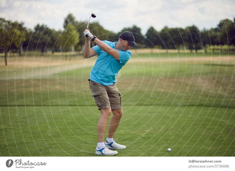 Mann, der Golf spielt und den Ball schwingt, während er seinen Schlag mit einem von hinten gesehenen Driver ausführt, der in einem gesunden, aktiven Lebensstilkonzept das Fairway hinunterblickt