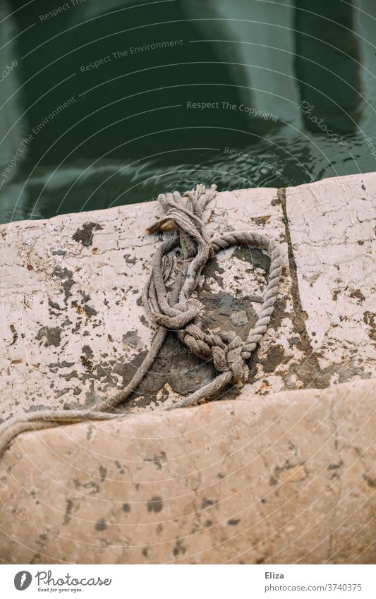 Ein Hanfseil mit Knoten auf einer Stufe am Ufer eines Kanals Schiffstau maritim Seil Tau Hafen Schifffahrt Festmacherleine Leine fest Sicherheit Wasser