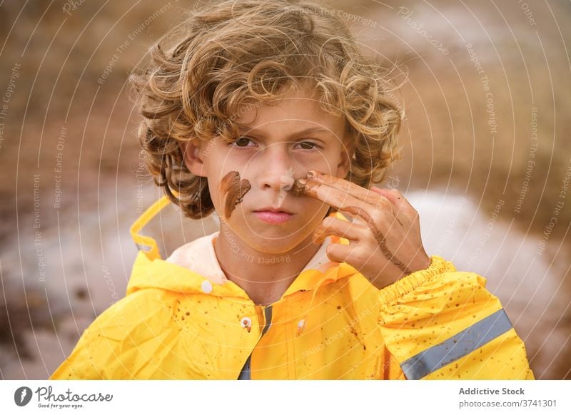 Junge im Regenmantel Zeichnung Zeichen auf seinem Gesicht mit dem Schlamm mit Blick auf die Kamera ernst Witz Stolz Säugling unordentlich geistig spielerisch