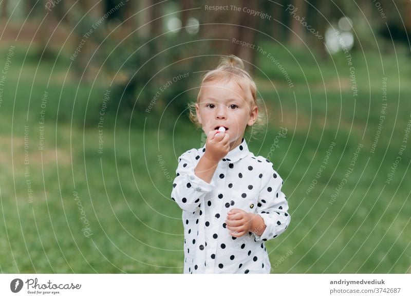 Das süße Mädchen schminkt sich mit Lippenstift und amüsiert sich im Wald, im Park. Das Konzept der Sommerferien, der Tag des Babys. Die Familie verbringt gemeinsam Zeit in der Natur.