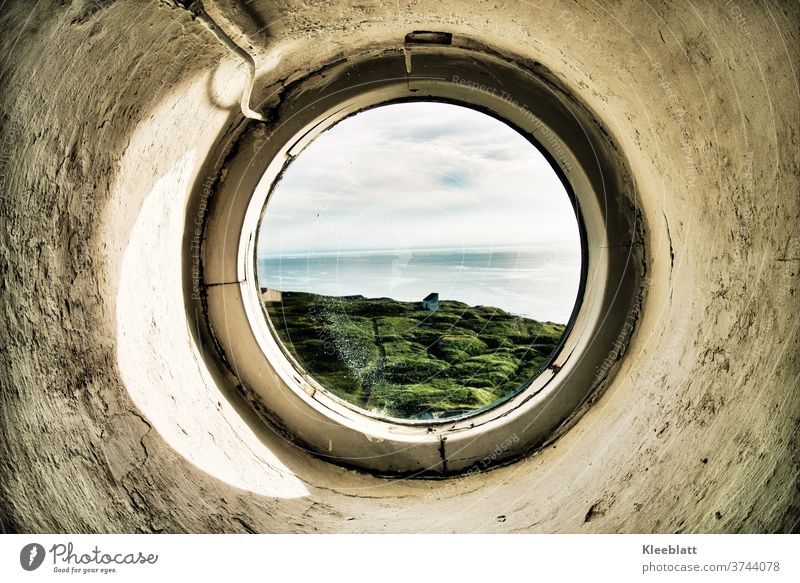 Durch ein rundes Bullauge des Leuchtturms den Blick auf's Meer gerichtet rundes Fenster grob verputzte Wand grau-weiße Farbe altes Fenter Blick aufs Meer