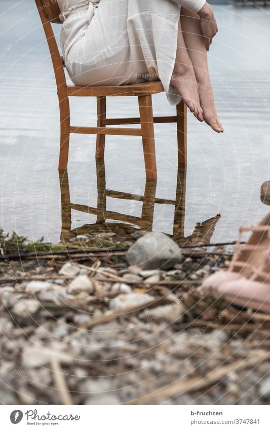 Frau sitzend auf Holzstuhl im Wasser Stuhl Sessel Sitzgelegenheit Möbel alt Einsamkeit braun Erholung ruhig warten Außenaufnahme Seeufer Steine Spiegelung Kleid