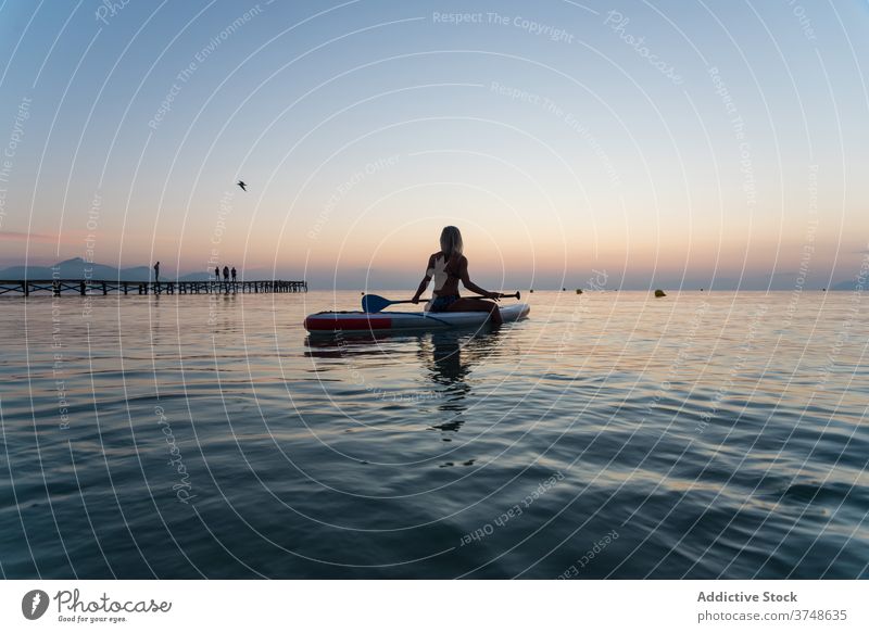 Anonyme Frau übt auf Paddleboard bei Sonnenuntergang Paddelbrett Surfer Zusatzplatine Reihe MEER Training Surfbrett Sommer Holzplatte sportlich sitzen