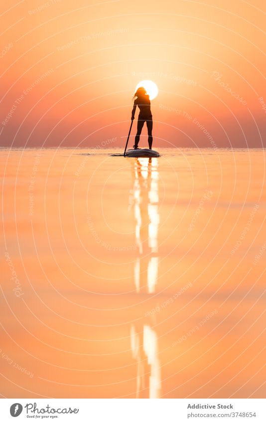 Anonyme Frau übt auf Paddleboard bei Sonnenuntergang Paddelbrett Surfer Zusatzplatine Silhouette Reihe MEER Training Surfbrett Sommer Holzplatte sportlich