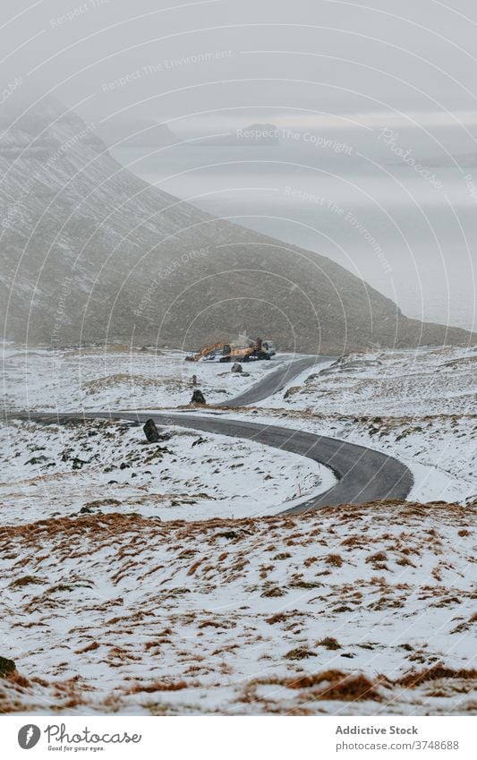 Straße in den Bergen auf den Färöer Inseln Asphalt Berge u. Gebirge Schnee Landschaft leer Natur Winter kalt Fahrbahn wolkig Hügel Ausflug Wetter Saison Weg