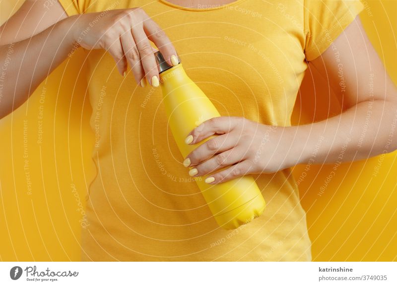 Nahaufnahme einer Frau, die eine gelbe wiederverwendbare Flasche auf gelbem Hintergrund hält Hand Monochrom ökologisch Wasser Stahl Thermo offen Halt hell