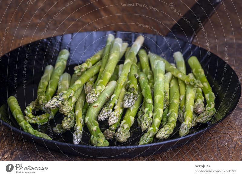 frischer grüner Spargel in einer Pfanne auf dunklem Holz Eisenpfanne Planke Saison saisonal Gourmet String Küche Zutaten Antioxidans gesund Essen Sprossen