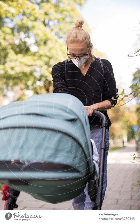 Besorgte junge Mutter, die auf einer leeren Straße mit einem Kinderwagen unterwegs ist und medizinische Masken trägt, die sie vor dem Coronavirus schützen sollen. Sozial distanziertes Leben während einer Coronavirus-Pandemie