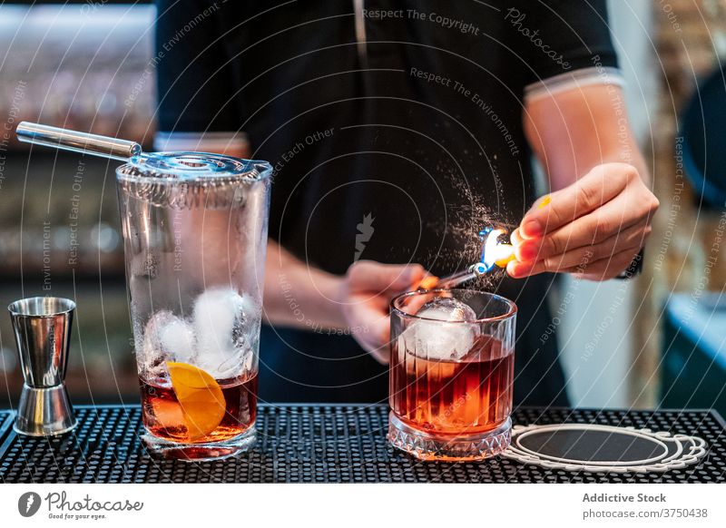 Crop Barmann bereitet Cocktail in Bar negroni vorbereiten Barkeeper Mann Feuer Flamme orange trinken männlich Abfertigungsschalter Scheibe Getränk Restaurant