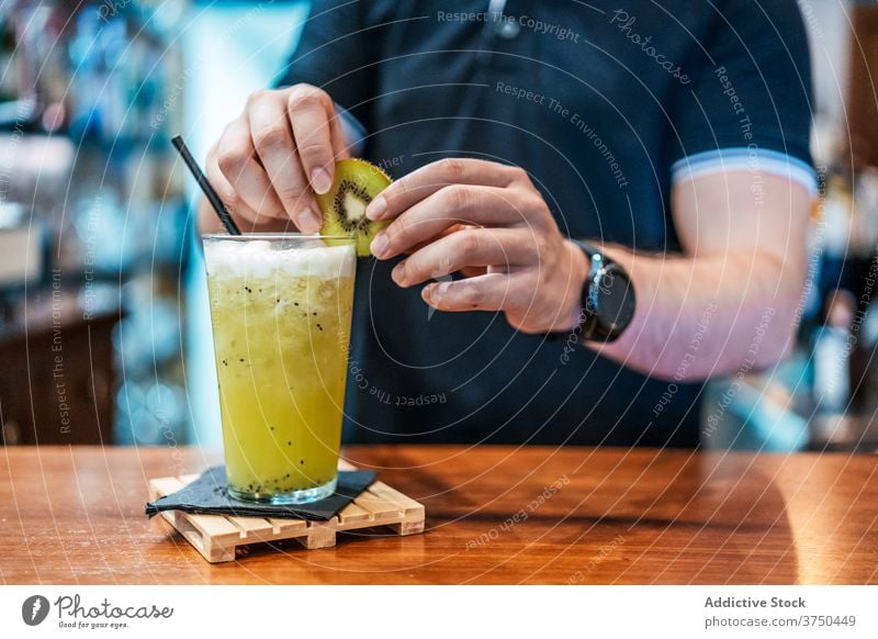 Crop Barmann bereitet Cocktail am Tresen alkoholfrei vorbereiten Barkeeper Frucht Kiwi Garnierung kalt Erfrischung männlich Glas Scheibe trinken Getränk lecker