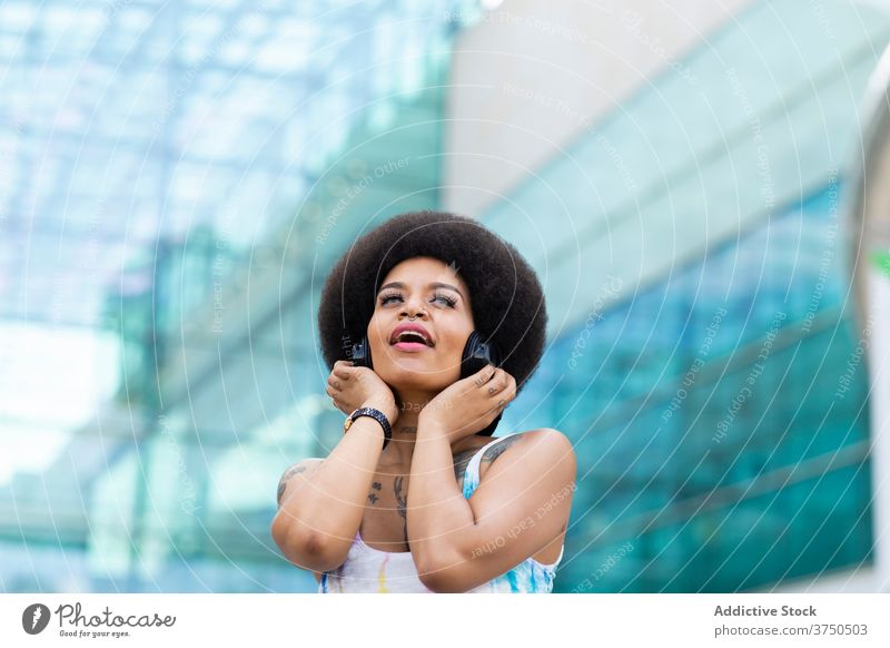 Verträumte schwarze Frau, die mit Kopfhörern Musik hört zuhören verträumt sorgenfrei genießen Gesang Großstadt urban ethnisch Afroamerikaner Afro-Look Frisur