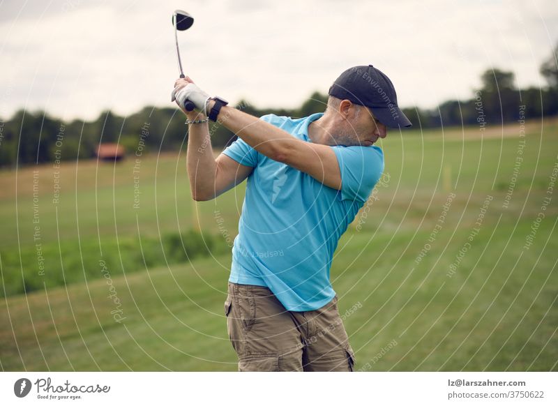 Mann, der Golf spielt und den Ball schwingt, während er seinen Schlag mit einem von hinten gesehenen Driver ausführt, der in einem gesunden, aktiven Lebensstilkonzept das Fairway hinunterblickt