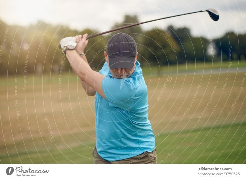 Mann, der Golf spielt und den Ball schwingt, während er seinen Schlag mit einem von hinten gesehenen Driver ausführt, der in einem gesunden, aktiven Lebensstilkonzept das Fairway hinunterblickt