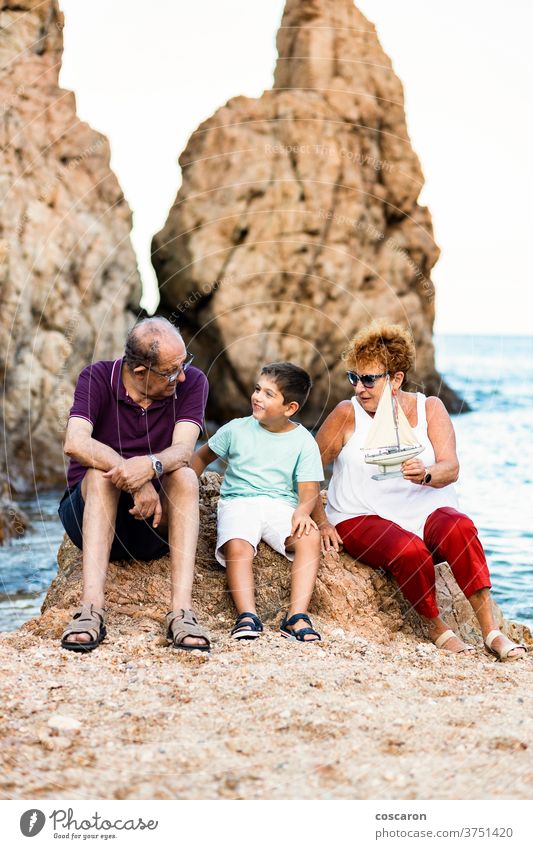 Großeltern und Enkel spielen mit einem Spielzeugsegelboot am Strand Boot Junge Kaukasier Kind Kindheit Küste Küstenlinie niedlich Familie Großvater Großmutter