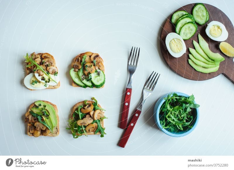 verschiedene vegetarische Toasts am Morgen, die mit Pilzen, Avocado, Rucola, Gurke und Eiern serviert werden. Gesundes Essen auf weißem Hintergrund Zuprosten