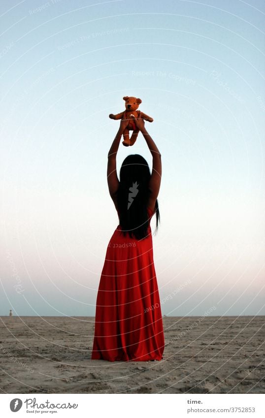 spirit in a material world abend stimmung dunkelhaarig langhaarig kleid strand himmel nordsee rot elegant weiblich halten frau teddy kinderspielzeug stofftier