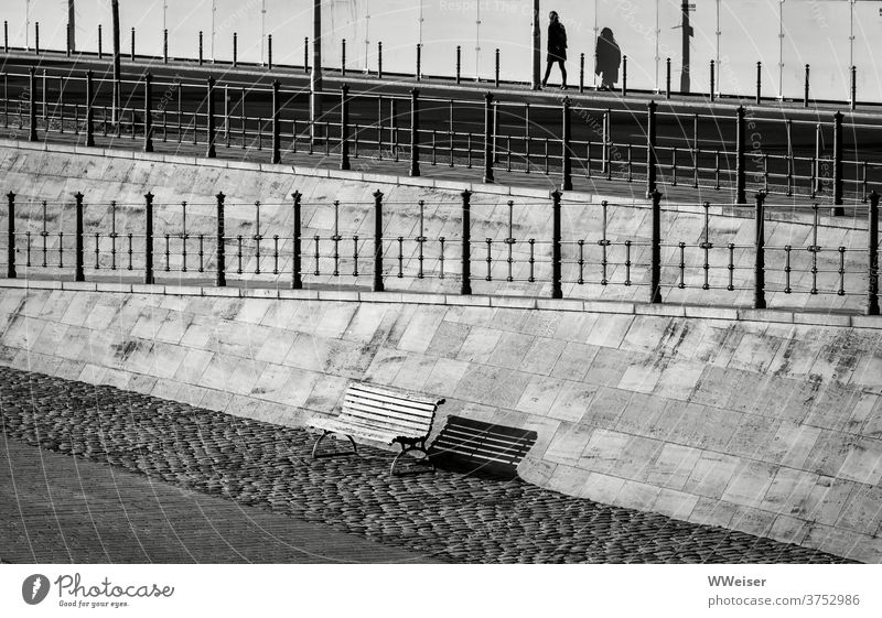 Am Berliner Spreebogen geht eine Frau fort, eine Bank bleibt leer zurück Ufer Promenade Stadt Straße Geländer Schatten Licht Diagonale Poller Pfosten Passant