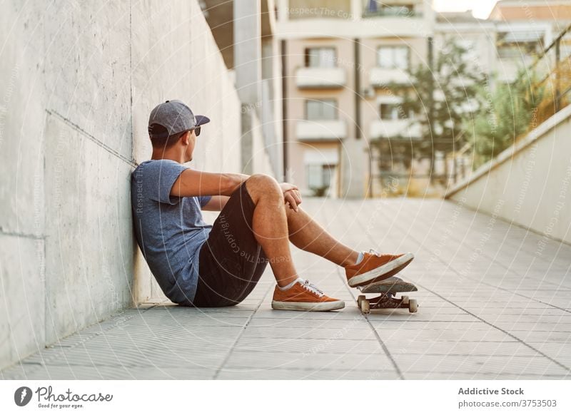 Stilvoller Mann mit Skateboard in der Stadt Skater urban Gebäude Hobby Fähigkeit fettarm Wand männlich Outfit selbstbewusst trendy Straße modern jung Großstadt