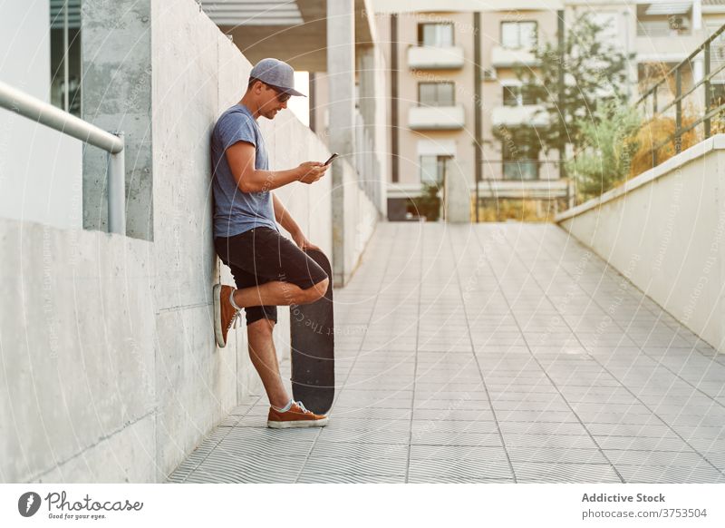 Männlicher Skater beim Surfen auf dem Smartphone in der Stadt Mann Skateboard Großstadt benutzend Straße Gebäude urban Stil männlich Apparatur Gerät Mobile jung