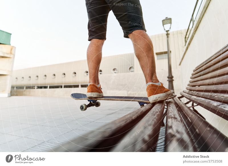 Crop Skater macht Trick auf Bank in der Stadt Skateboard Mann Großstadt Hobby Stunt Schlittschuh urban Stil männlich Fähigkeit Talent Turnschuh hölzern cool