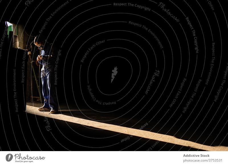 Anonymer Arbeiter in Uniform in der Garage Mechaniker Atemschutzgerät dunkel Sonnenstrahlen professionell Job behüten stehen Sicherheit Gerät Dienst Beruf