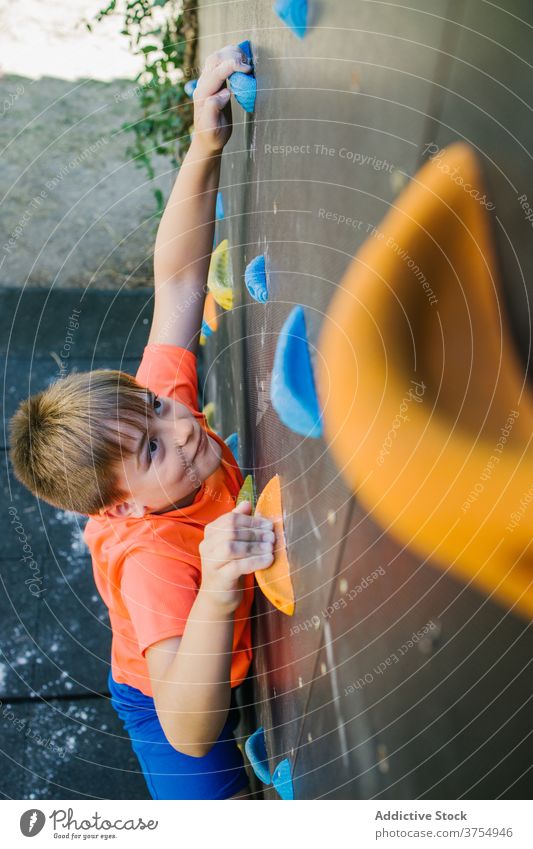 Mutiger Junge klettert an der Wand in der Turnhalle Aufstieg Kind Felsbrocken Fitnessstudio Training Griff Gleichgewicht Halt furchtlos üben Übung extrem Hobby