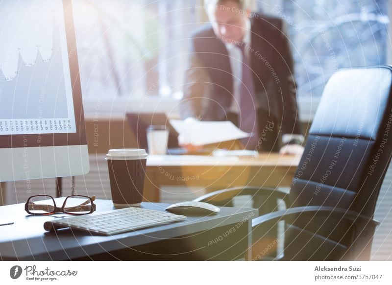 Nahaufnahme eines Büroschreibtisches mit Computer, Tastatur, Brille und Tasse Kaffee. Geschäftsmann im Anzug arbeitet mit Dokument im Hintergrund Schreibtisch